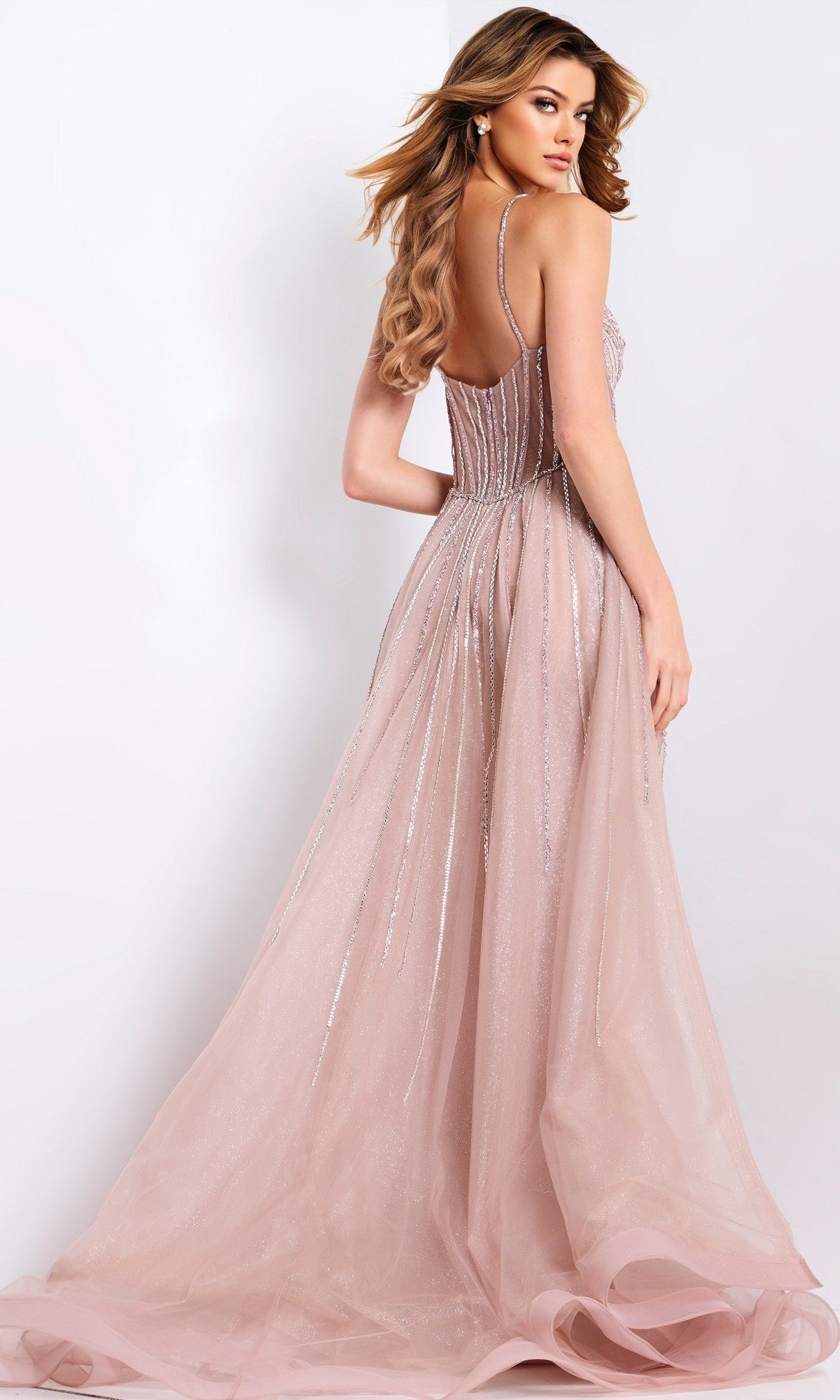 A woman wears the Jovani 43854 long prom dress—a sleeveless, backless blush pink gown with sparkling details and a corset bodice—standing against a white background and looking over her shoulder.